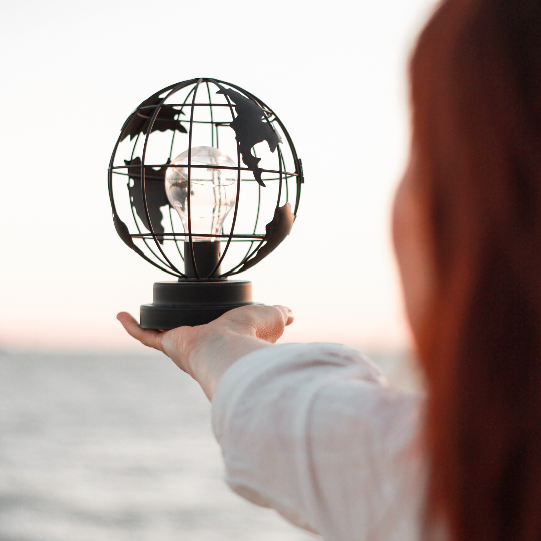 Charlotte TREMEL tournant son regard vers l'horizon, tenant une lumière en forme de monde dans sa main, représentant l'accompagnement et la vision globale pour les entreprises en transformation.